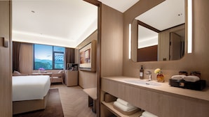 Een moderne hotelkamer met een groot bed, een bank, een bureau en een badkamer met wastafel, spiegel en toiletartikelen.