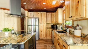 Eine Küche mit Holzausstattung, einem Edelstahlkühlschrank, Granit Arbeitsplatten und einer Holzzieldecke.