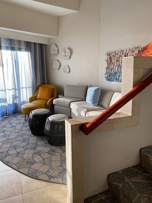 Ein Wohnzimmer mit Sofa, Sesseln, Hocker und einer Treppe.