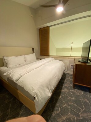 Ein Hotelzimmer mit Bett, Fernseher, Fenster und einem hölzernen Kopfteil.