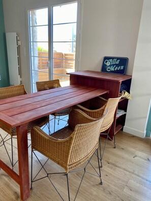 Ein Essbereich mit einem Holztisch, Korbstühlen, einem Schild mit der Aufschrift 'Villa Moon' und Blick durch eine Glastür auf eine Außenpatio.