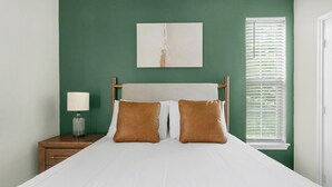 A bedroom with a bed, nightstand, lamp, and a window with blinds. - Landing | Stylish 1BD in Copperfield (Cypress)