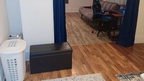 Ein Zimmer mit einem Bett, einem Schreibtisch mit Stuhl, einem Mülleimer und einem gemusterten Teppich.