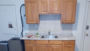Eine Küche mit Holzschränken, einer Granitarbeitsplatte, einem Edelstahlspülbecken und einem Mülleimer.
