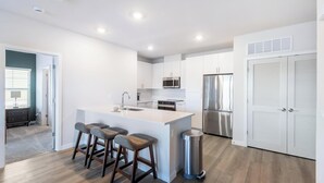Et moderne køkken med en central ø, barstole, rustfrie stålapparater og en skraldespand.