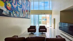 A spacious lobby with a large abstract painting, two leather chairs, a glass partition, and a view of the outside. - COARM0114 - Acqua Vert Loft Residence (Salvador)