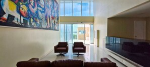 A spacious lobby with a large abstract painting, two leather chairs, a glass partition, and a view of the outside.