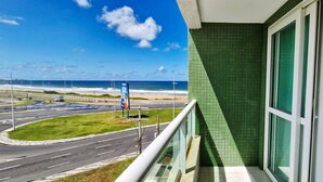 A balcony with a view of a road and beach, a green tiled wall, and a window with a white frame. - COARM0114 - Acqua Vert Loft Residence (Salvador)