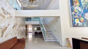 A hotel lobby with a marble wall, a staircase, a sofa, and a large abstract painting. - COARM0114 - Acqua Vert Loft Residence (Salvador)