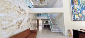 A hotel lobby with a marble wall, a staircase, a sofa, and a large abstract painting.