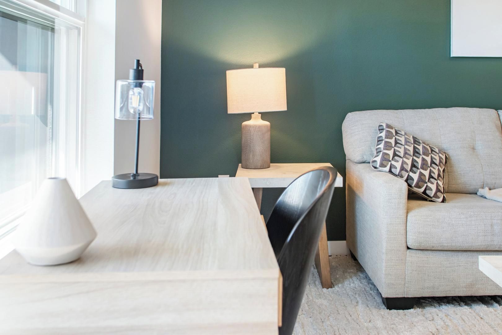 Ein modernes Wohnzimmer mit Esstisch, einer Couch mit gemusterten Kissen, einer Lampe und einem an der Wand befestigten Regal.