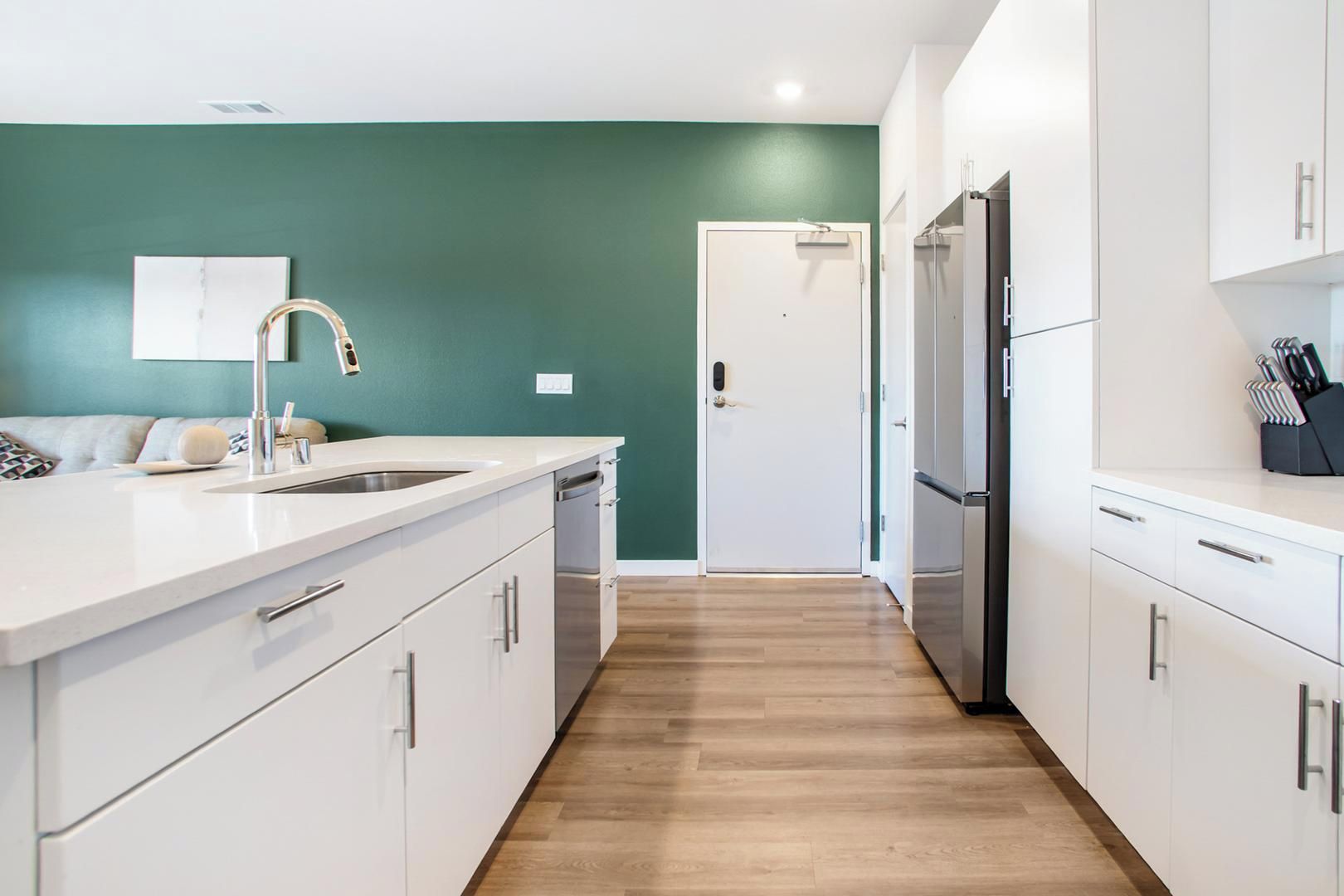 A modern kitchen with white cabinetry, a stainless steel sink, and a refrigerator.