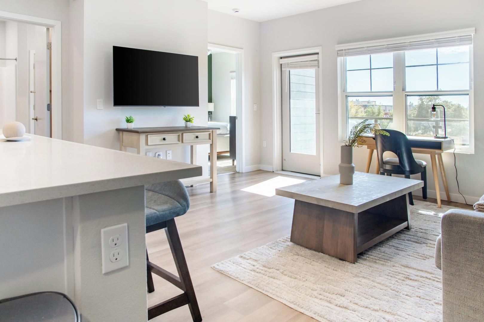 Una cocina moderna con una isla grande, un comedor con mesa y sillas, y una sala de estar con sofá y televisor.
