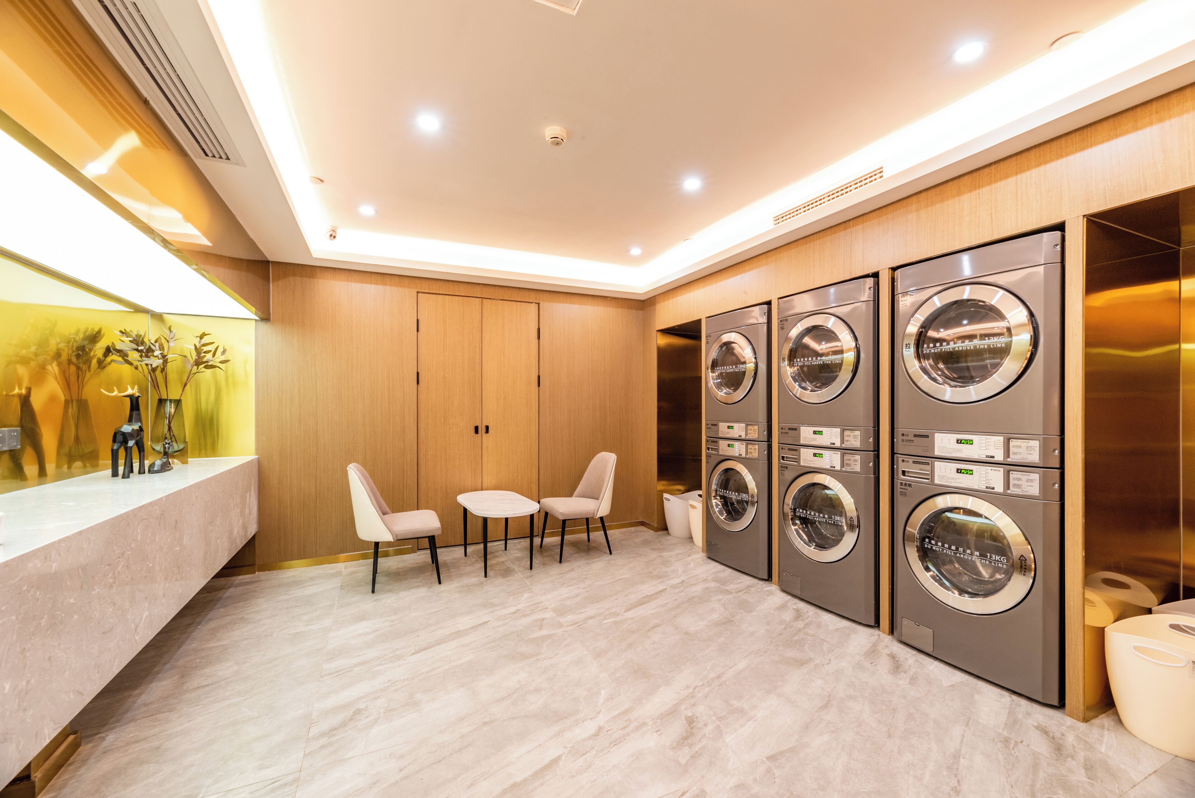 A modern laundry room with four washing machines, a marble floor, and a seating area with two chairs.