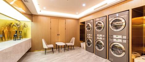 A modern laundry room with four washing machines, a marble floor, and a seating area with two chairs.