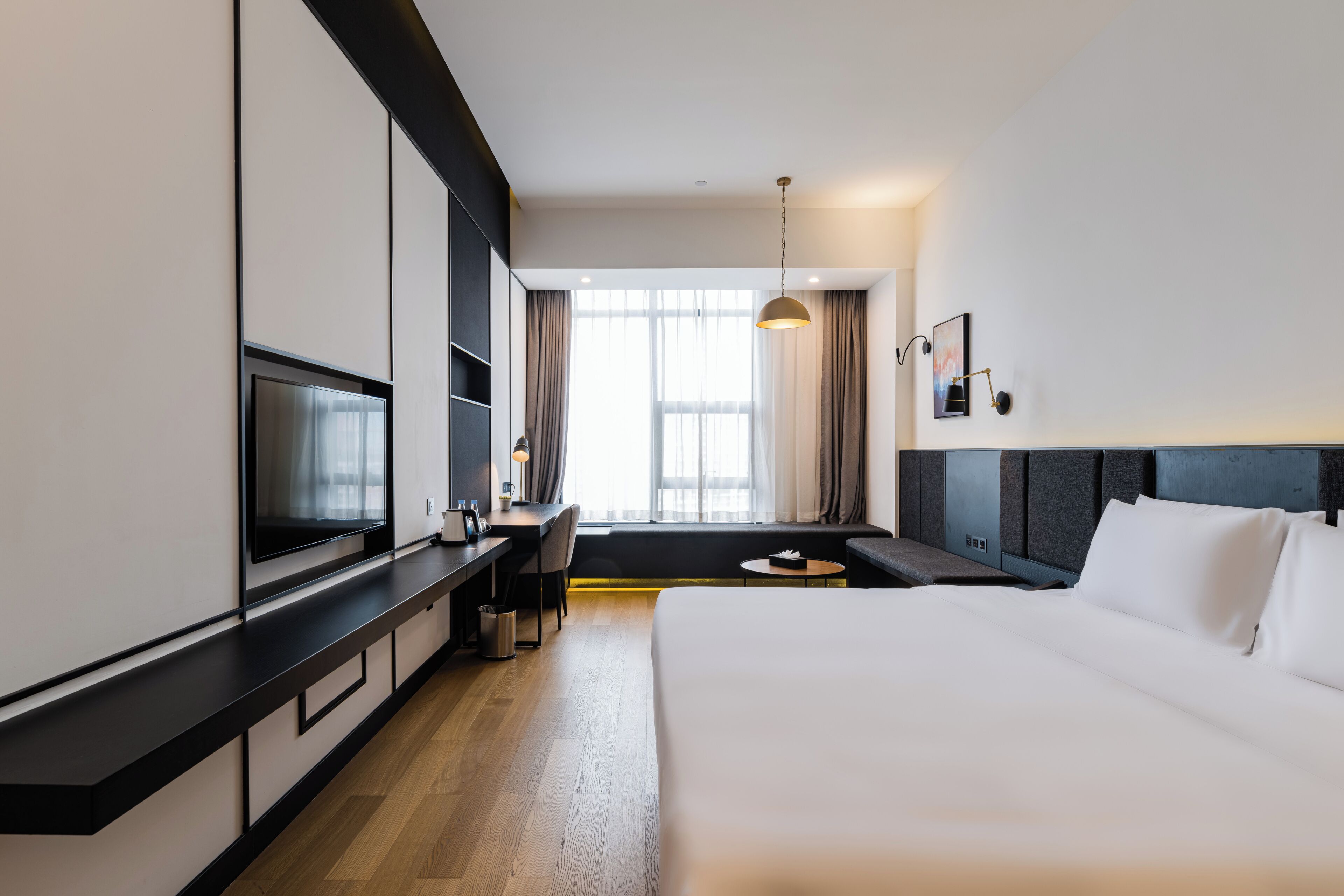 Una habitación de hotel moderna con una cama, un escritorio, un televisor y un amplio ventanal.