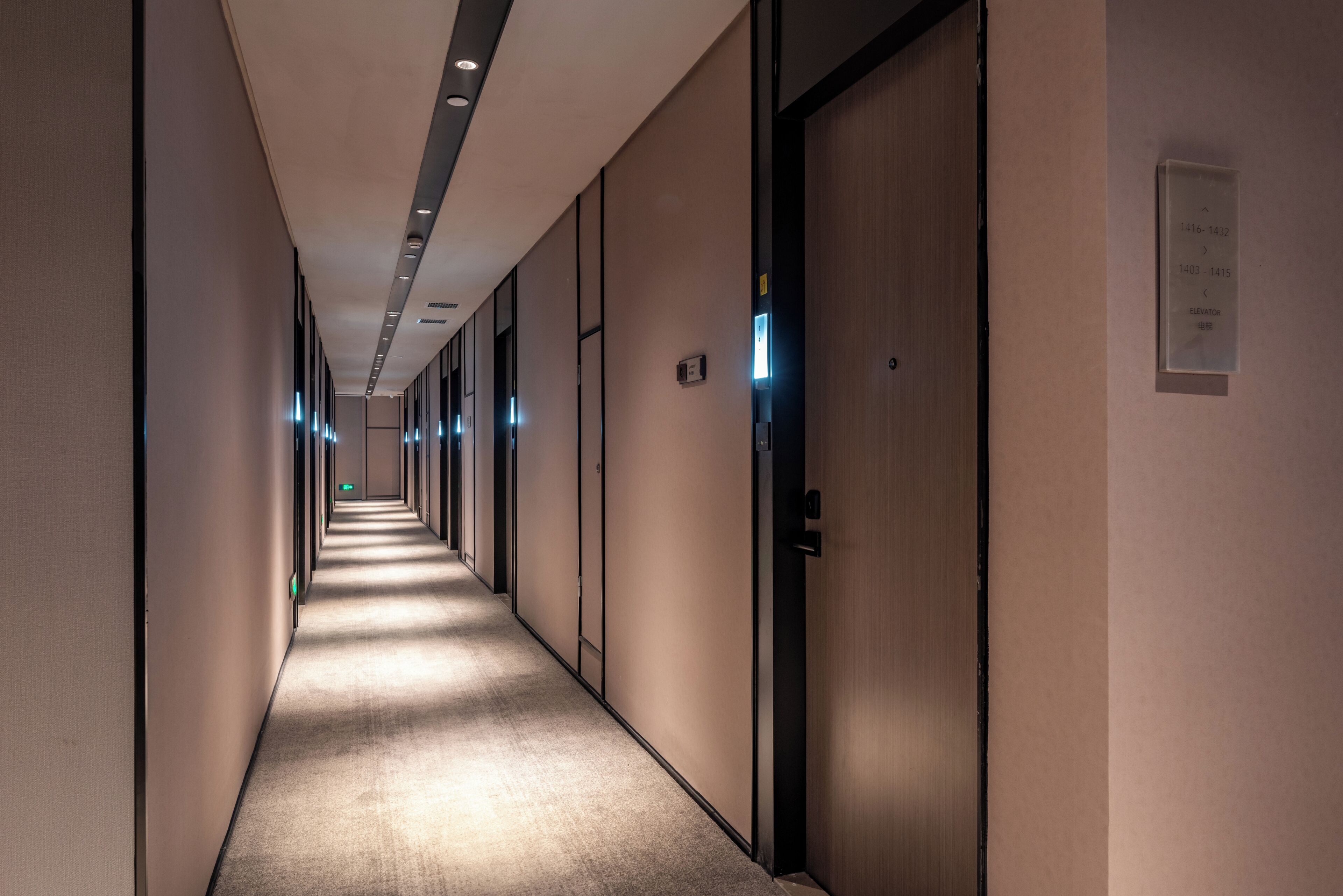A long, narrow hotel corridor with doors on one side and a carpeted floor.