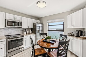 A modern kitchen with white cabinets, stainless steel appliances, a dining table with chairs, and a view of the sea. - Top Floor Marco Island Waterfront Condo with heated pool (Marco Island)