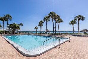 A swimming pool with a clear view of the ocean, surrounded by palm trees and lounge chairs. - Top Floor Marco Island Waterfront Condo with heated pool (Marco Island)