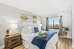 A bedroom with a bed, bedside tables, a window with curtains, and a view. - Top Floor Marco Island Waterfront Condo with heated pool (Marco Island)