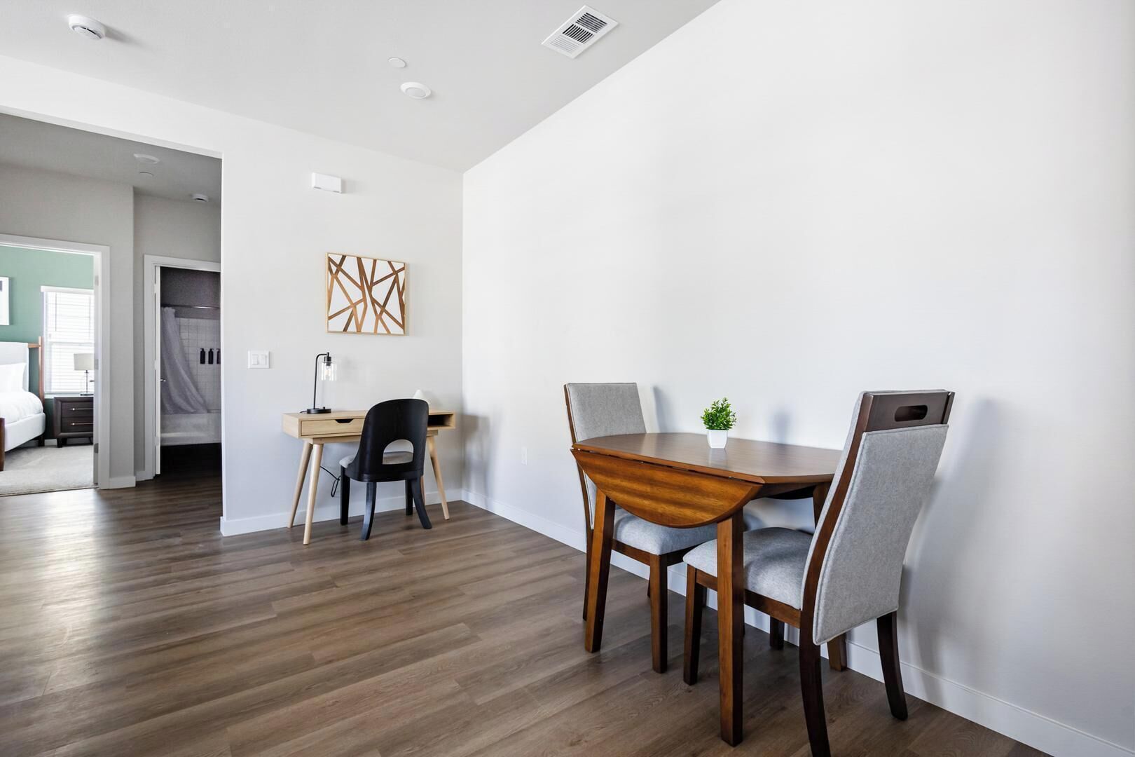 Una habitación moderna con una mesa de comedor de madera y sillas, un escritorio con una silla, una cama y un cabina de ducha.