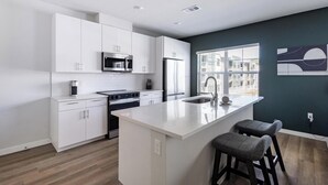 Una cocina moderna con muebles blancos, electrodomésticos de acero inoxidable, una isla grande con taburetes y vistas a través de una ventana.