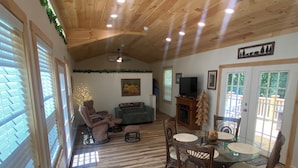 A spacious living area with a wooden ceiling, a fireplace, a television, and a dining table with chairs. - Hudlow Hideaway…A perfect and secluded couple’s getaway with hot tub! (Union Mills)