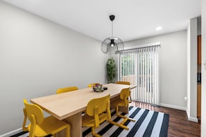 Un coin repas avec une table en bois et des chaises jaunes, un luminaire suspendu noir et une vue sur l’extérieur grâce à une porte coulissante.