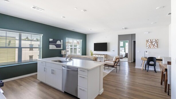Cozinha moderna com ilha central, área de jantar com mesa e cadeiras, e sala de estar com cama e televisão.