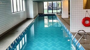 Een binnenzwembad met betegelde muren, helderblauw water en een reddingsboei aan de rechterkant.