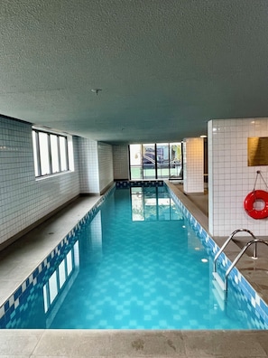 Ein Hallenbad mit gefliesten Wänden, einem klaren blauen Becken und einem Rettungsring rechts.