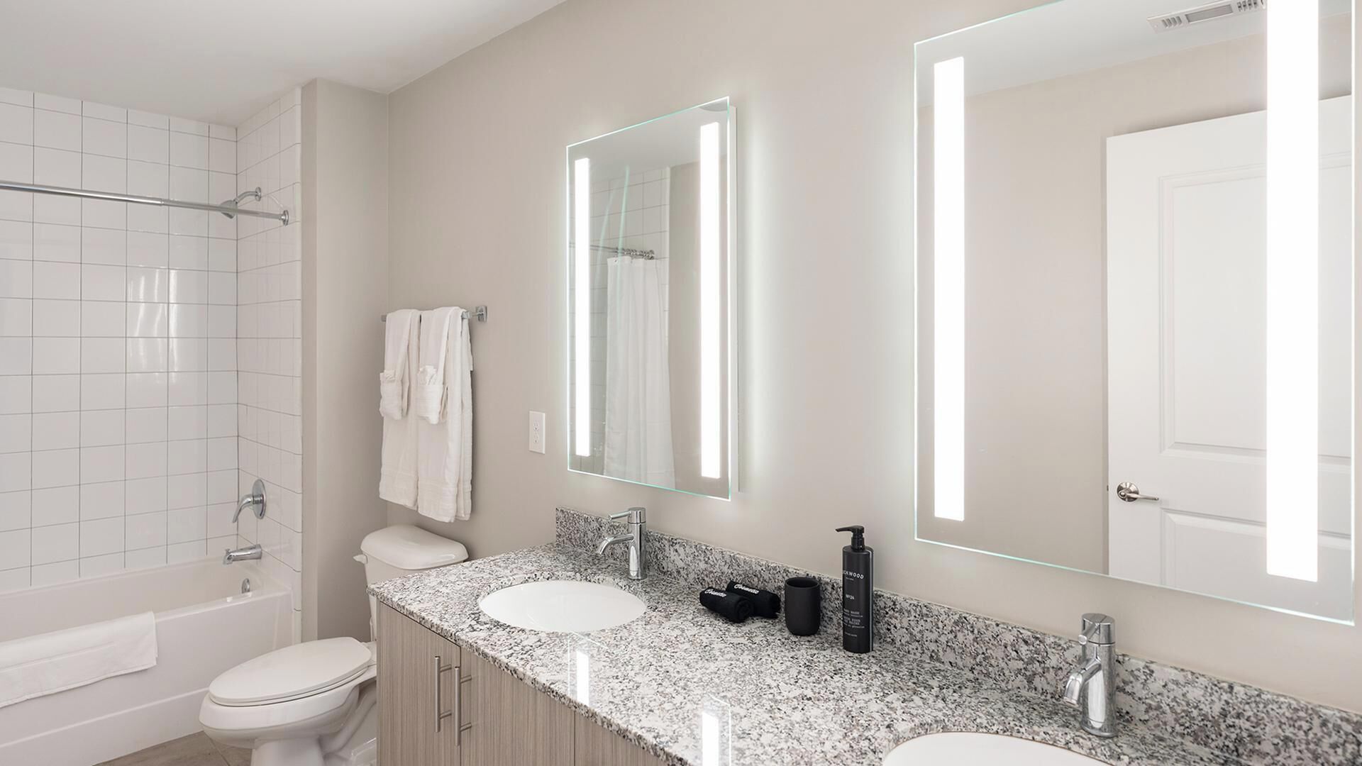 A modern bathroom with a bathtub, two sinks, a large mirror, and a toilet.