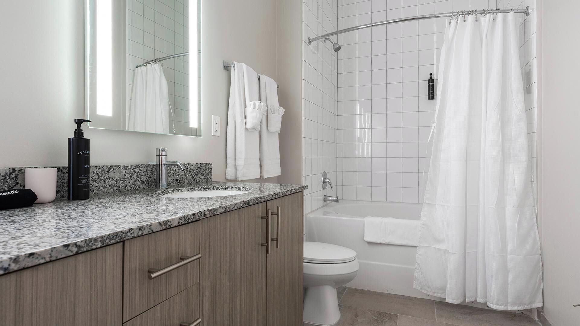 Un baño moderno con encimera de granito, inodoro, bañera y cortina de ducha.
