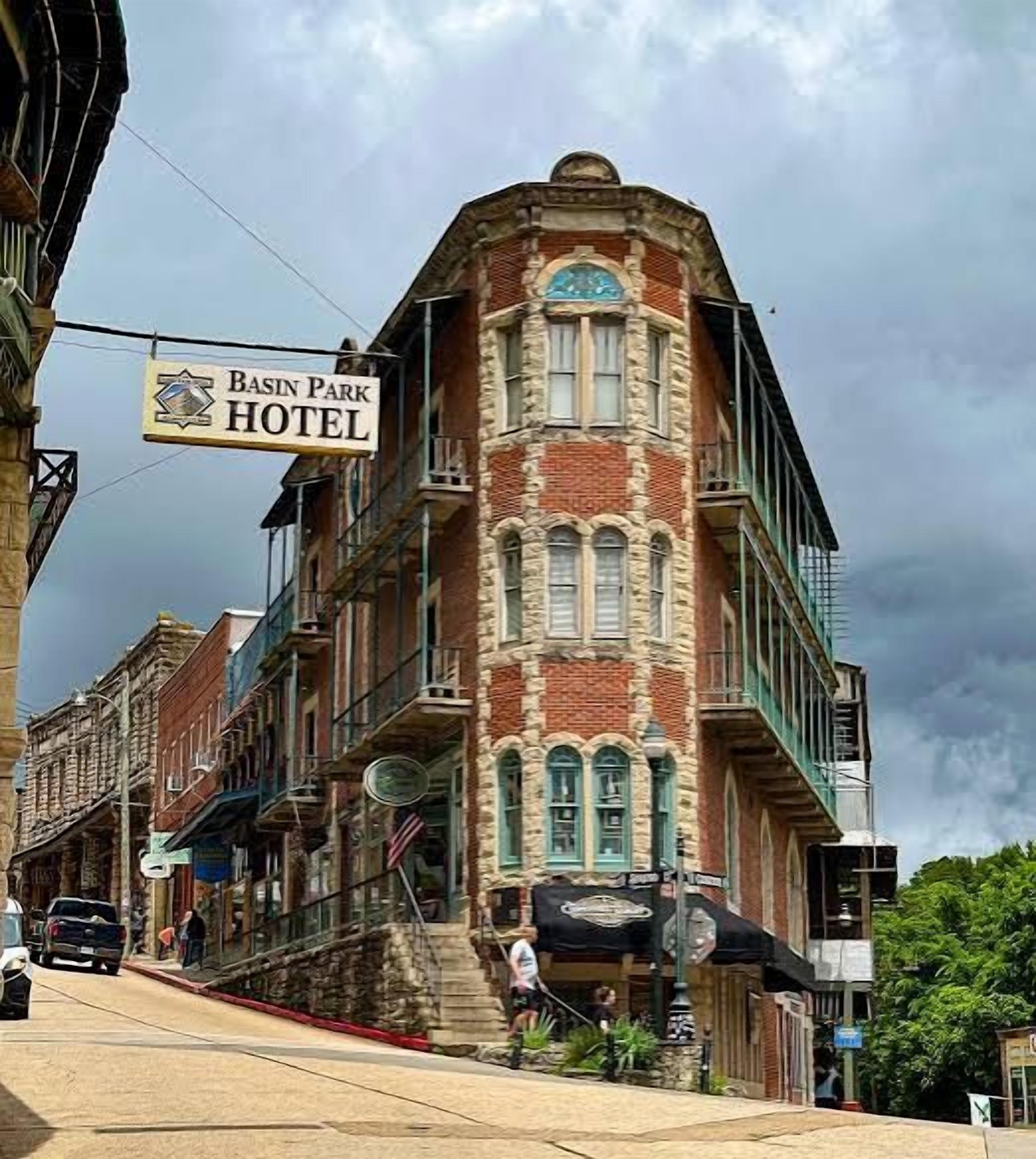 A historic hotel with a prominent corner building, a sign indicating it's the Basin Park Hotel, and a street-level bar.