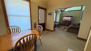 Ein Essbereich mit Holztisch und Stühlen, ein Wohnzimmer mit Fernseher und ein Fenster mit Jalousien.