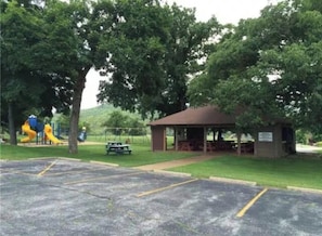 Un parque con un pabellón, mesas de picnic y un parque infantil.