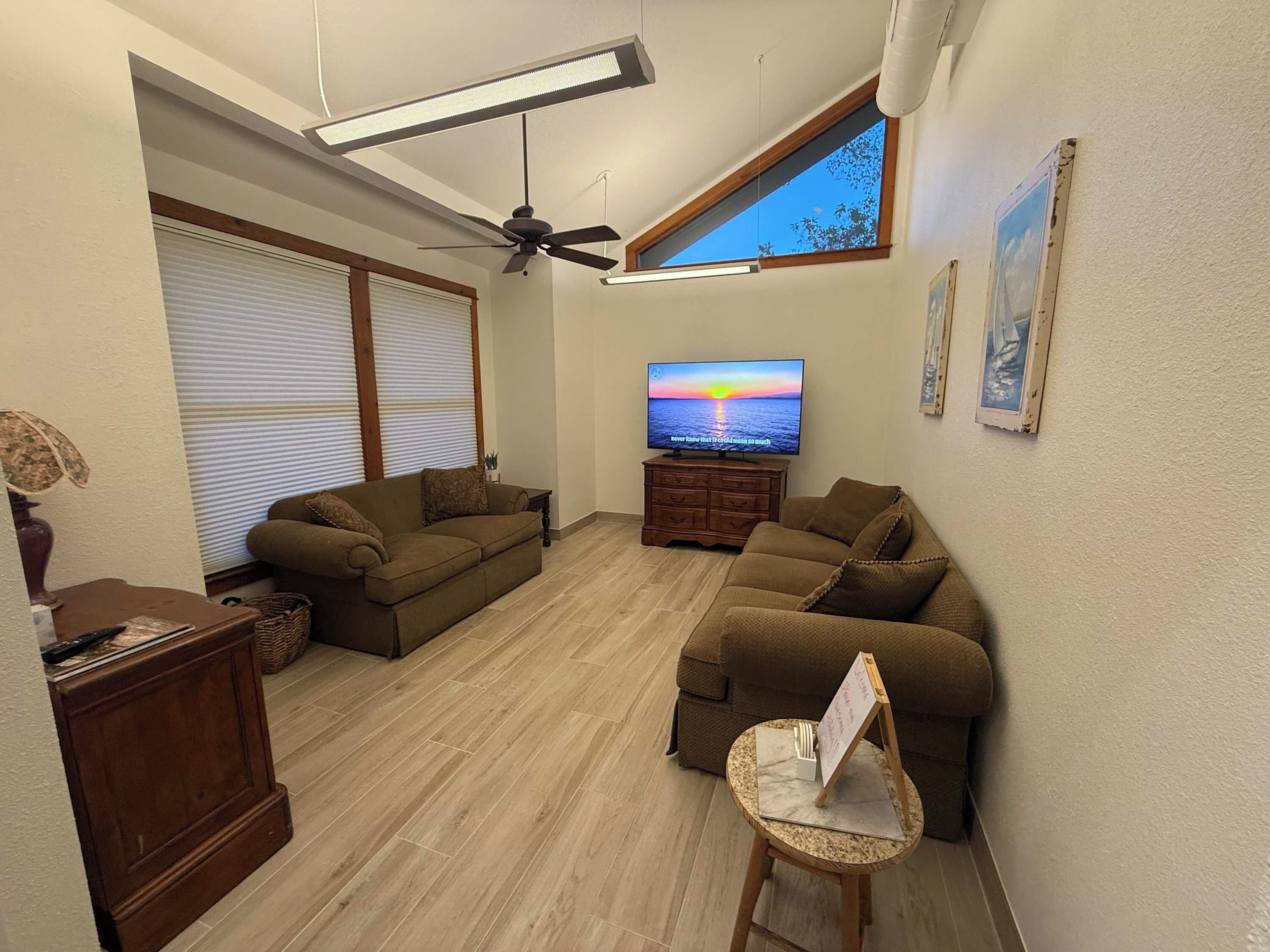 Ein Wohnzimmer mit Deckenventilator, Flachbildfernseher und großem Fenster.