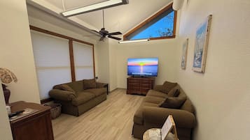 Ein Wohnzimmer mit Deckenventilator, Flachbildfernseher und großem Fenster.