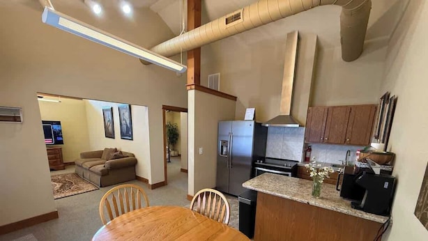Eine moderne Küche mit einer zentralen Kochinsel, ein Essbereich mit Holztisch und Stühlen sowie ein Wohnzimmer mit Sofa und Fernseher.