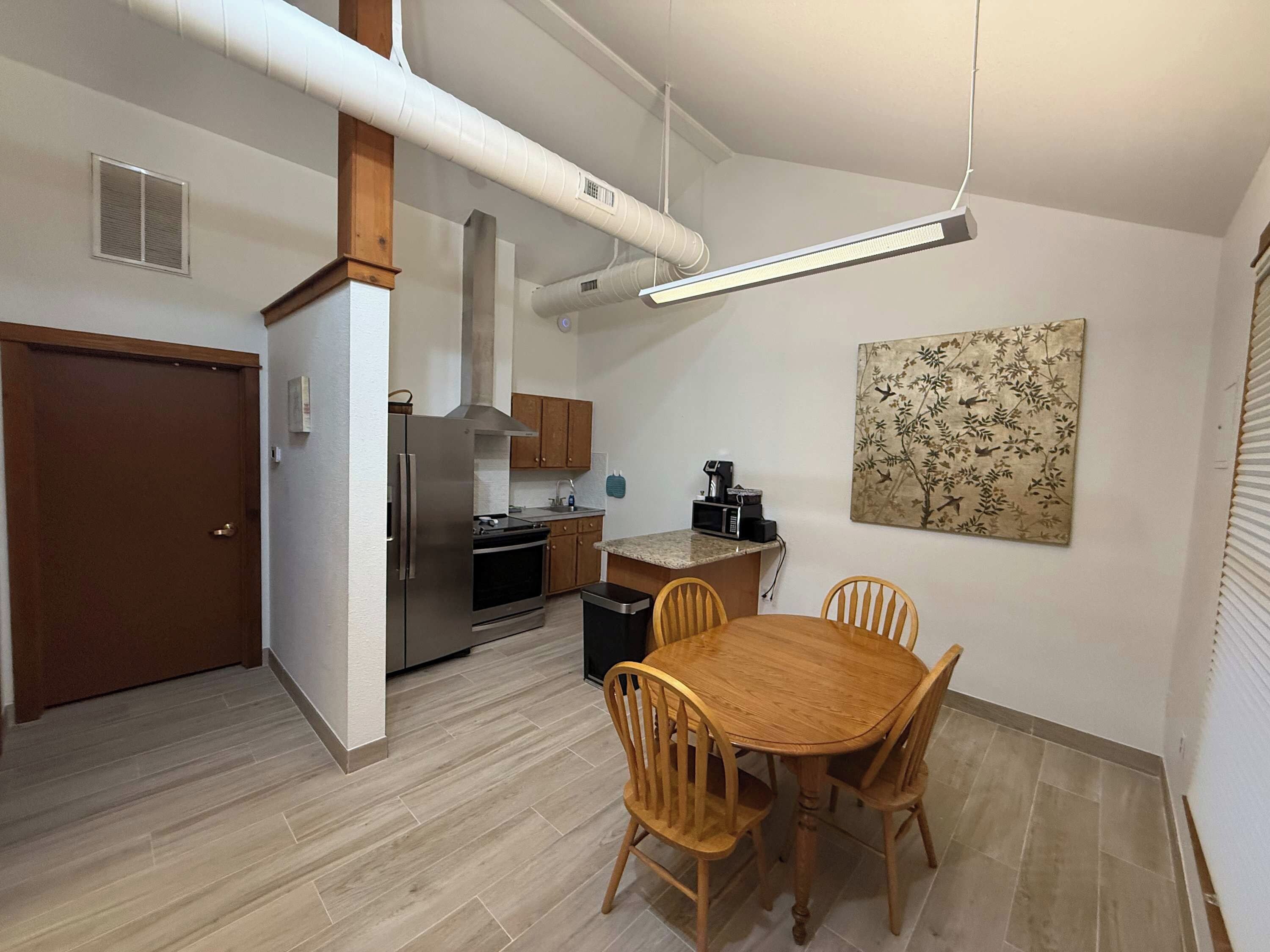 A compact kitchen with modern appliances, a dining area with a wooden table and chairs, and a decorative wall piece.