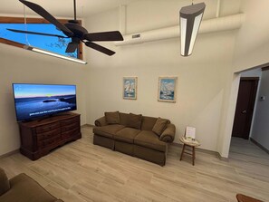 Una sala de estar con una televisión de pantalla plana, un ventilador de techo y dos cuadros en la pared.