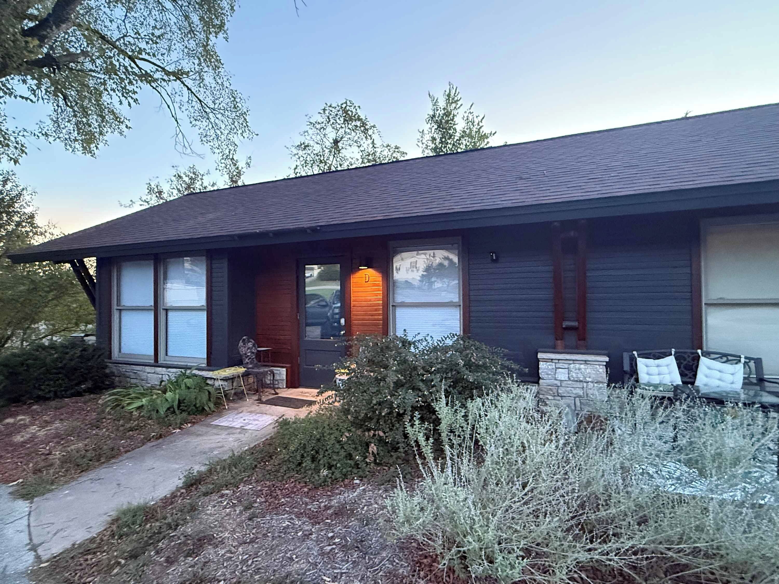 A two-story house with a dark roof, a front porch with a bench, and a small garden area.