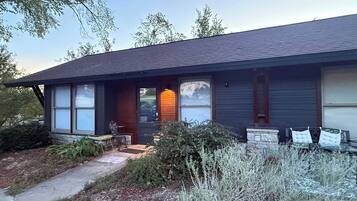 A two-story house with a dark roof, a front porch with a bench, and a small garden area.