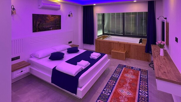 A modern bedroom with a bed, a small sitting area, a window, and a bathroom.