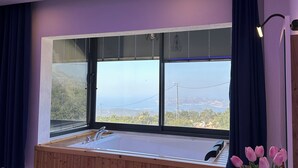 A modern bathroom with a large window, wooden bench, and a small table.