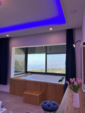 A modern bathroom with a large window, wooden bench, and a small table.