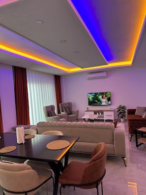 A modern living room with a sofa, chairs, a dining table, and a TV.