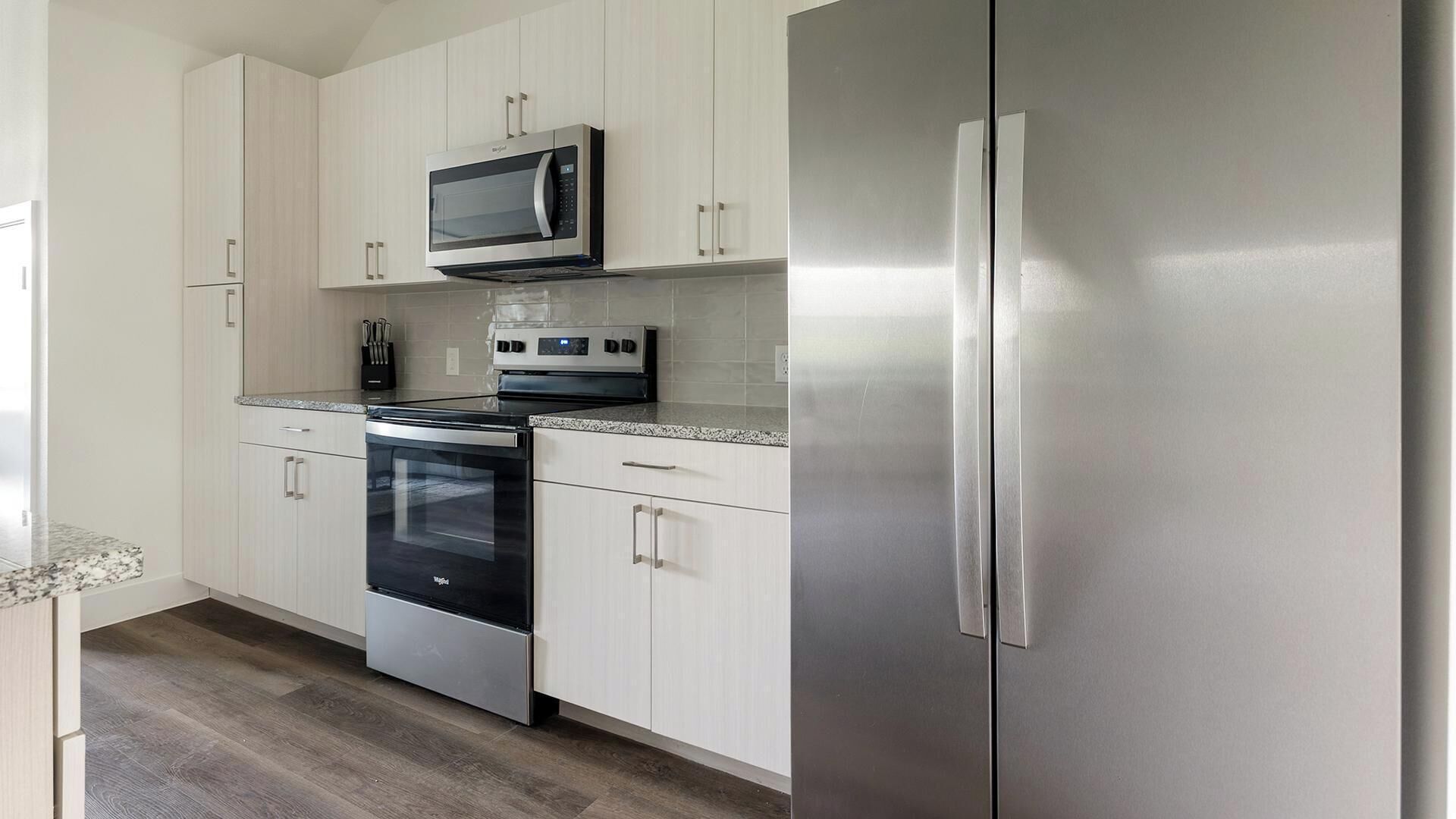 A kitchen with white cabinets, a stainless steel refrigerator, a microwave, a stove, and a dishwasher.