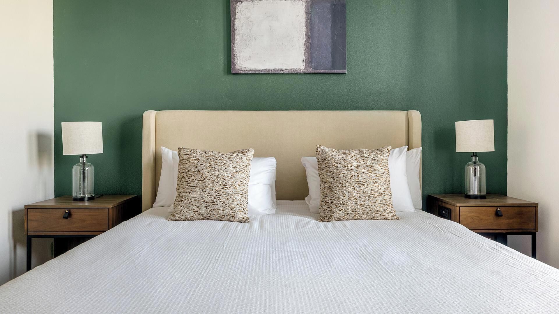 A bed with two pillows, a nightstand with a lamp, and a painting on the wall.