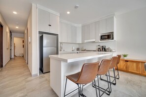Eine moderne Küche mit weißen Schränken, einem Edelstahl-Kühlschrank, einer Mikrowelle und einer Bar mit Hockern.